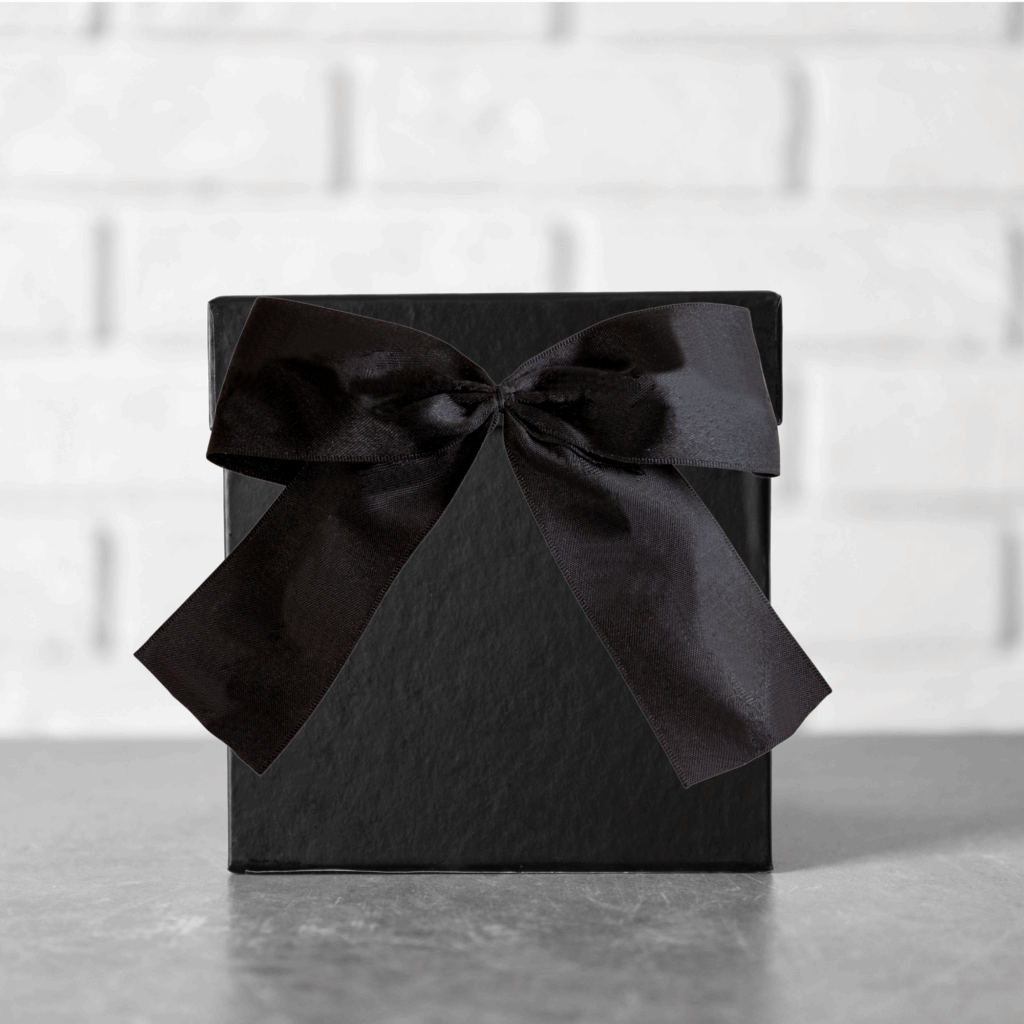 A black box with a black bow against a grey brick wall.