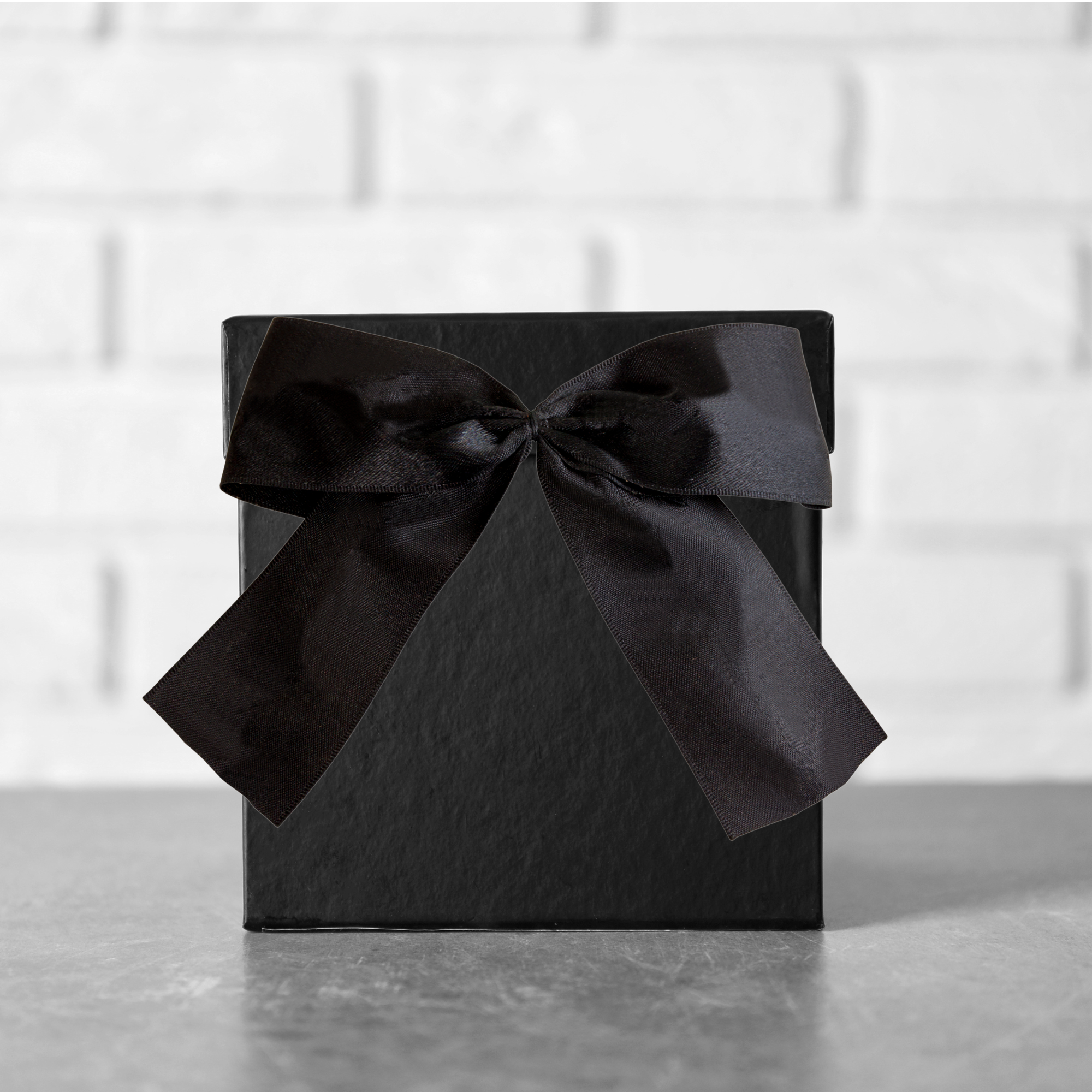 A black box with a black bow against a grey brick wall.